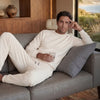 Man in a white outfit sitting on a couch in a modern living room with a scenic view.