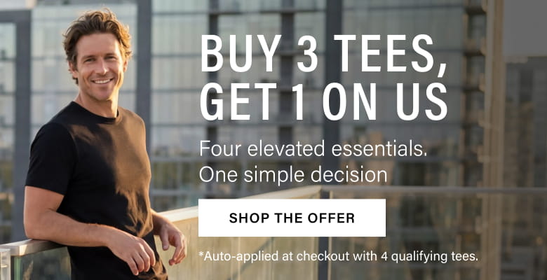 Man wearing a black t-shirt standing against a blurred cityscape background. Promotional text reads: Buy 3 Tees, Get 1 On Us. Four elevated essentials. One simple decision. Shop the Offer. Auto-applied at checkout with 4 qualifying tees.